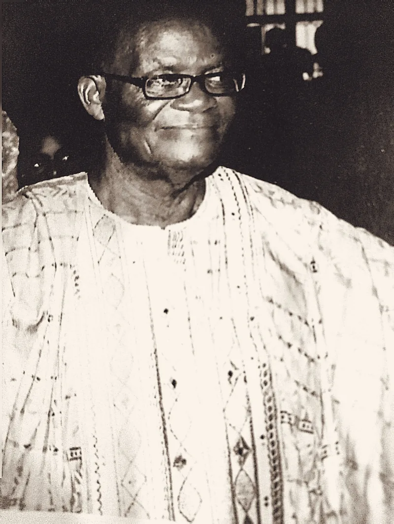 Papa Elkanah Osibanjo standing in patterned adire, at an evening gathering.